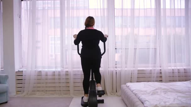 モデル 脂肪の女性は 自宅で静止自転車に従事 — ストック動画