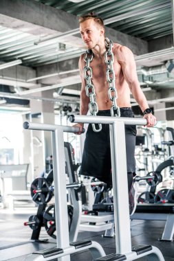 Boynunda kocaman metal bir zincir olan sporcu. Spor salonundaki yamuk barlarda şınav.