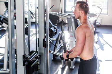 Spor salonunda triseps yapan genç kaslı bir adamın fotoğrafı.