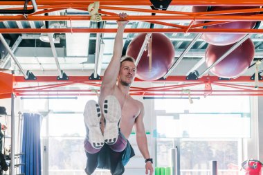 Strong shirtless male athlete shows calisthenic moves Hanging on pull bar one arm leg raises or l-sit hold clipart