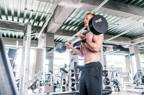 Sport, Bodybuilding, Lifestyle- und People-Konzept - junger Mann mit Langhantel lässt Muskeln im Fitnessstudio spielen — Stockfoto