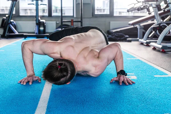 Un hombre desnudo del torso en el gimnasio hace flexiones, tocando el suelo con su hombro — Foto de Stock