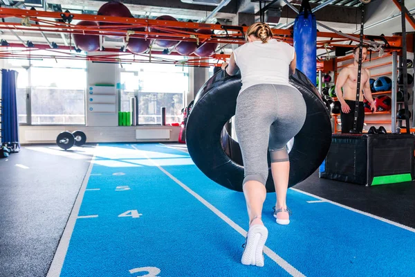 Ajuste atleta femenina haciendo ejercicio con un neumático enorme, girando y volteando en el gimnasio . — Foto de Stock