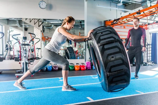 Ajuste atleta femenina haciendo ejercicio con un neumático enorme, girando y volteando en el gimnasio . — Foto de Stock