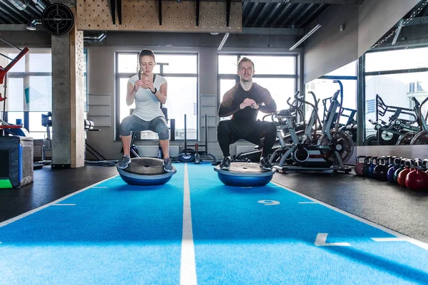 Ajuste pareja trabajando en la bola de bosu en el gimnasio. Haciendo un ejercicio en cuclillas — Foto de Stock