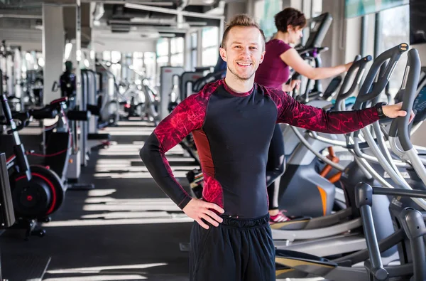 Young man - fitness instructor smiling and looking at the camera on the background of the gym