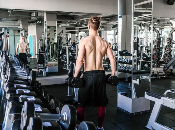 Sportlicher Mann mit nacktem Oberkörper im Fitnessstudio hebt Hanteln. — Stockfoto