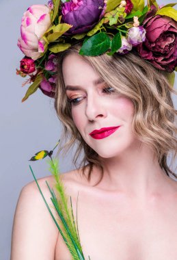 Yapay yeşil kelebekli çiçek çelenginde poz veren genç bir kadın, gri renkte izole edilmiş.