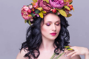 Yapay yeşil kelebekli çiçek çelengi içinde poz veren narin, genç esmer kadın, menekşe arka planda izole edilmiş.