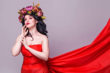 Kafasında parlak çiçekler, mor arka planda uzun kırmızı elbisesi olan güzel esmer kadın model.