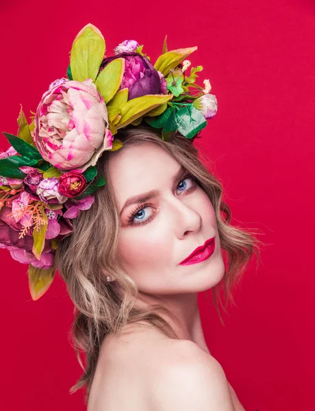 Красивая молодая женщина модель с яркими цветами на голове на красном фоне — стоковое фото