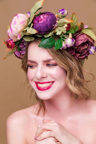 Happy beautiful young woman model with bright flowers on her head smile on the ocher color background