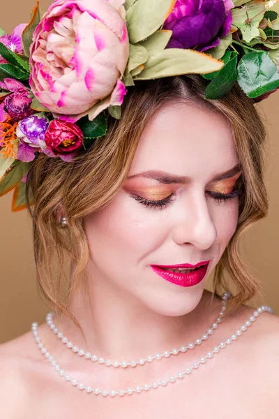 Hermosa modelo de mujer joven con flores brillantes en la cabeza con perlas en el fondo de color ocre —  Fotos de Stock