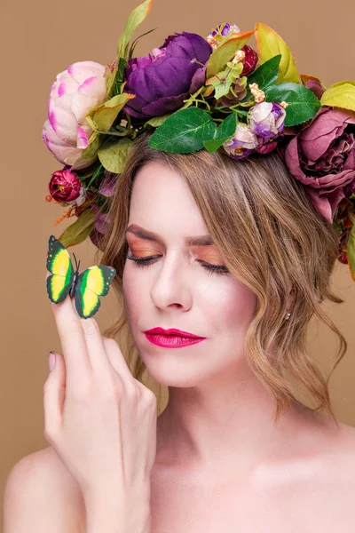 Tierna joven posando en corona de flores con mariposa verde artificial, aislada sobre fondo de ochet —  Fotos de Stock