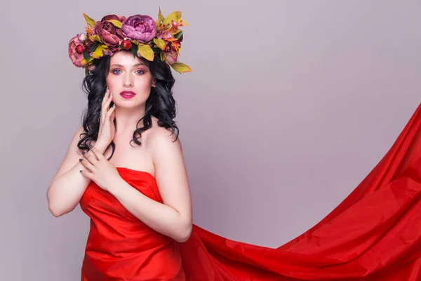 Красивая молодая брюнетка женщина модель с яркими цветами на голове в длинном красном платье на фиолетовом фоне — стоковое фото