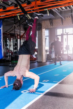 Spor salonunda baş aşağı duran bir sporcu. Elleriyle şınav çeken bir adam. Crossfit eğitimi. 