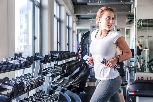 Jonge en mooie vrouw uit te werken met halters in sportschool — Stockfoto