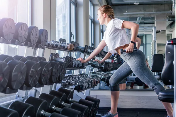 Jonge en mooie vrouw uit te werken met halters in sportschool — Stockfoto