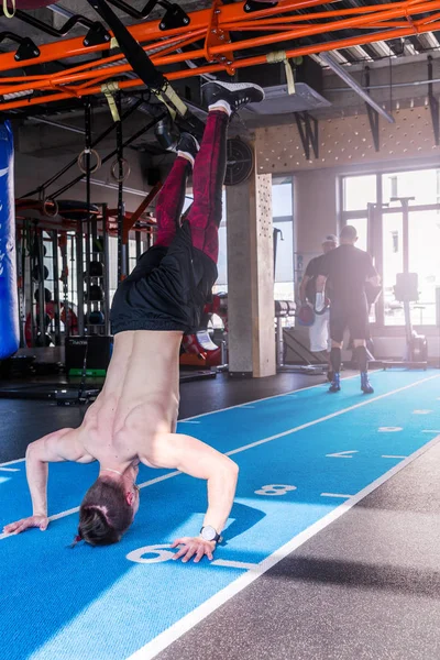 Athlete walking on his hands standing upside down in gym. Man doing push ups on his hands. Crossfit training.