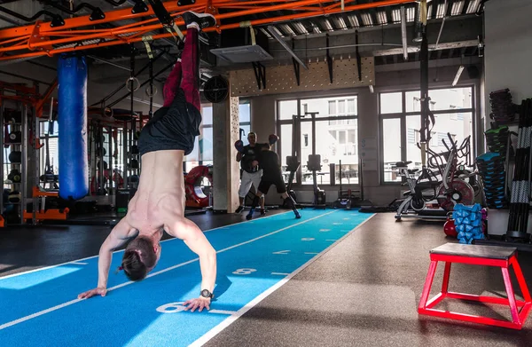 Athlete walking on his hands standing upside down in gym. Man doing push ups on his hands. Crossfit training.