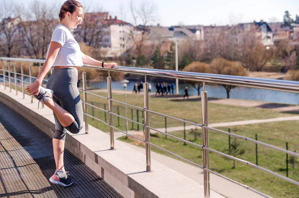 Temiz havada egzersiz yapmadan önce beyaz tişörtlü ve gri taytlı genç atletik kadın spor yapıyor..