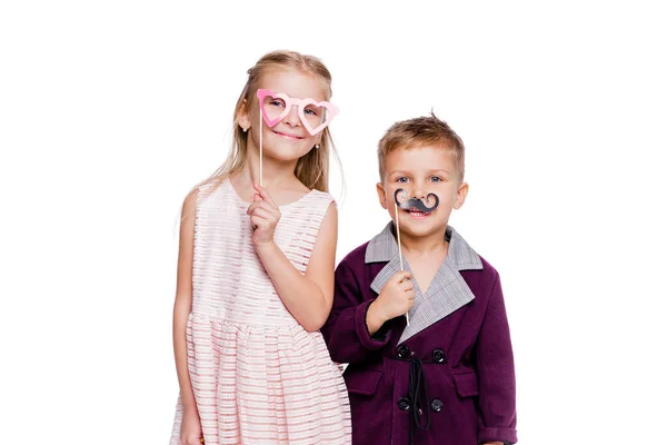 Chica con gafas de cartón en forma de corazón y un niño con un bigote de cartón posando sobre un fondo blanco —  Fotos de Stock