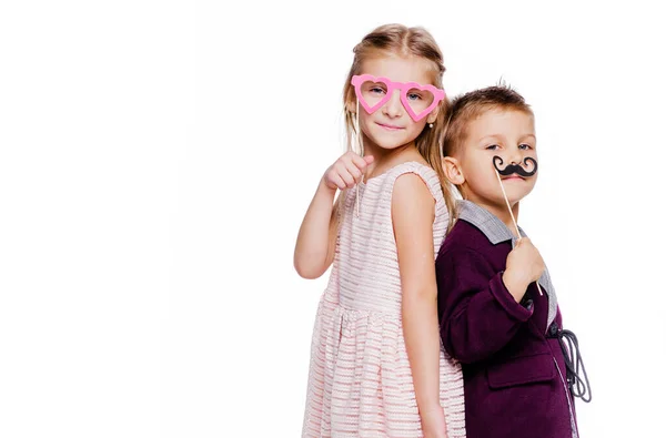 Chica con gafas de cartón en forma de corazón y un niño con un bigote de cartón posando sobre un fondo blanco —  Fotos de Stock
