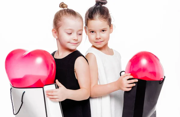 2 niñas con vestidos elegantes sostienen bolsas grandes con globos en forma de corazón en el interior —  Fotos de Stock