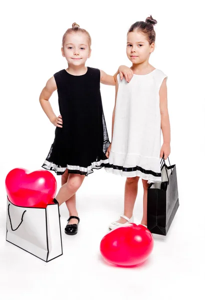 2 niñas con vestidos elegantes se quedan al lado de bolsos grandes con globos en forma de corazón en el interior —  Fotos de Stock