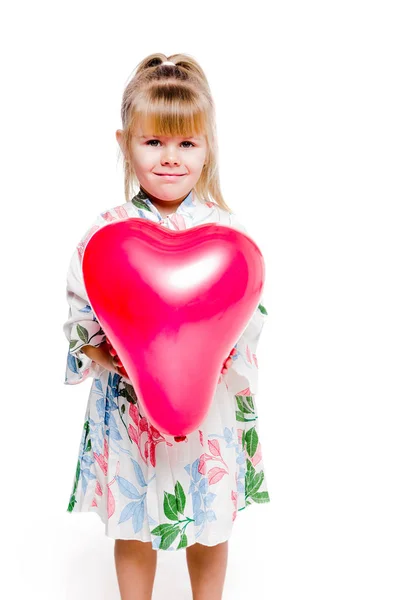 Menina em um vestido de impressão floral detém um balão em forma de coração vermelho em um fundo branco — Fotografia de Stock