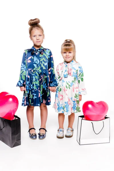 2 niñas con vestidos elegantes sostienen bolsas grandes con globos en forma de corazón en el interior —  Fotos de Stock