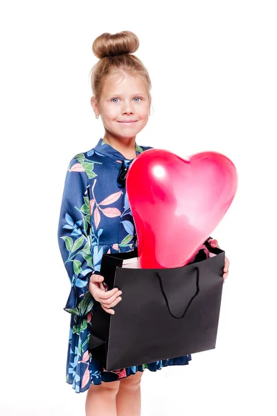 Pequeña chica de moda en un vestido floral azul sostiene una bolsa grande con un globo en forma de corazón en el interior —  Fotos de Stock