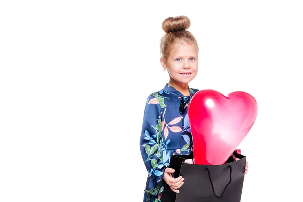 Pequeña chica de moda en un vestido floral azul sostiene una bolsa grande con un globo en forma de corazón en el interior —  Fotos de Stock
