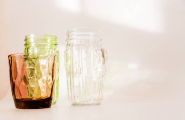 3 bardak - beyaz, kahverengi ve yeşil arka planda duruyor. Camdan geçen güneş ışığı ışığın kırılması sonucu beyaz zemin üzerinde güzel bir gölge oluşturur..