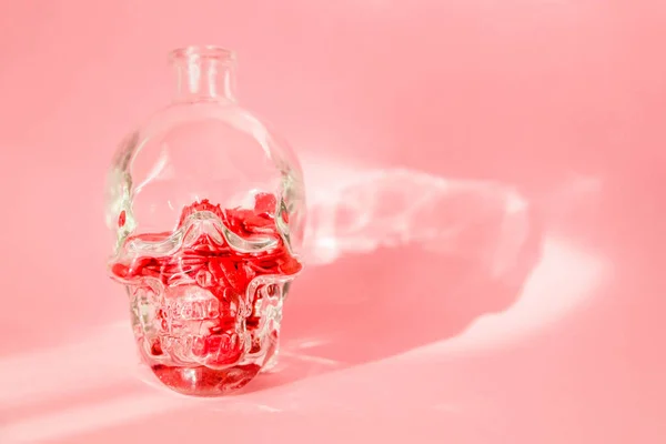 Uma garrafa de vidro na forma de um crânio humano é preenchido com corações vermelhos e fica em um fundo rosa — Fotografia de Stock