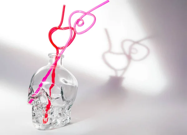 Tubos de coquetel em forma de coração em um decantador de vidro em forma de crânio em um fundo branco . — Fotografia de Stock