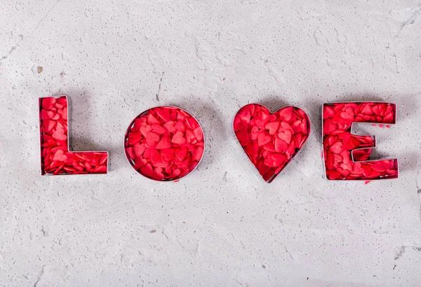 Inscription love made of red hearts on concrete background