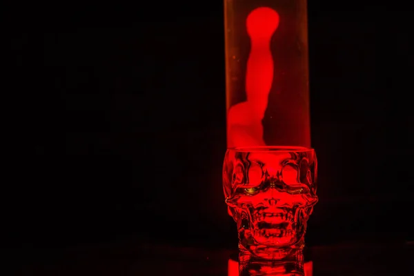 在黑色的背景上，一个人头骨形状的玻璃杯在红色的背景下反光. — 图库照片