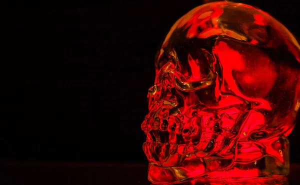 Glass skull crowned with red light on a black background