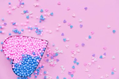 Pembe arka planda, metal bir kalp şekli dekoratif boncuklarla doludur..