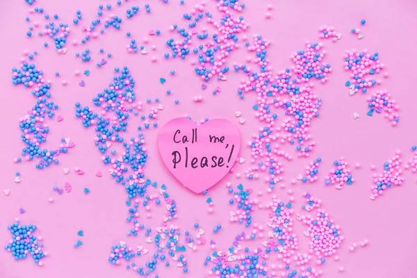 Paper pink heart on a background of decorative balls in blue and pink. There is a text on  heart call me please
