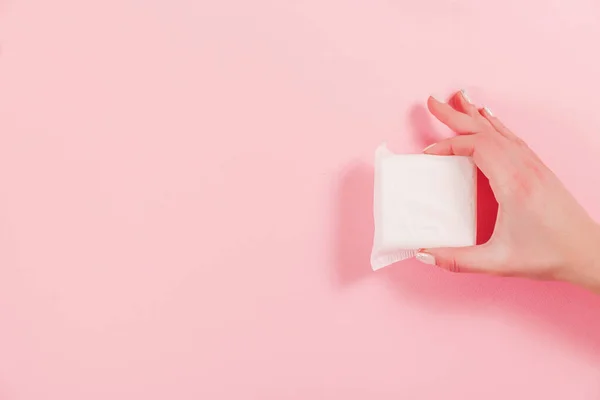Női kéz, amely rózsaszín alapon egészségügyi betétet tart — Stock Fotó