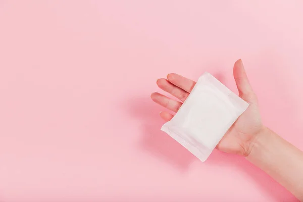Női kéz, amely rózsaszín alapon egészségügyi betétet tart — Stock Fotó