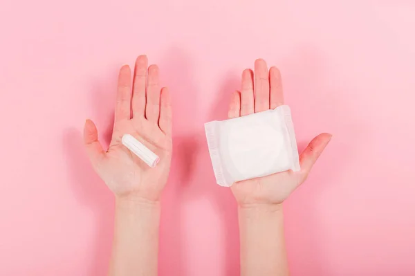 Női kéz tart egy egészségügyi pad és tampon rózsaszín alapon — Stock Fotó