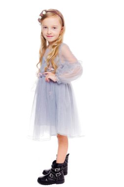 Kafasında çelenk, beyaz bir arka planda siyah çizmeleri olan gri elbiseli, şık kızıl saçlı küçük kız.