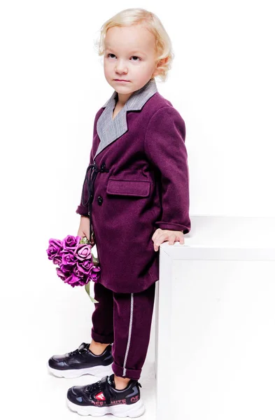 Pequeño niño de moda en un elegante traje de color burdeos y con un ramo de flores en sus manos sobre un fondo blanco. El chico está triste, molesto, enojado. — Foto de Stock