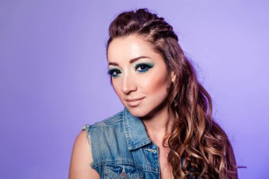 Beautiful brunette girl with blue makeup, pigtails and loose curly hair on a purple background