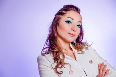 Beautiful brunette girl with make-up in blue tones, pigtails and in a white jacket posing on a background of purple