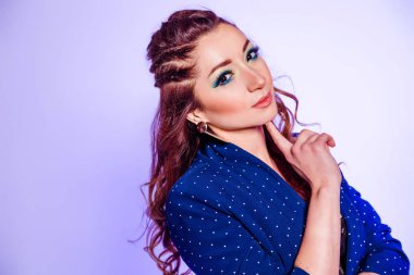 Beautiful brunette girl with make-up in blue tones, pigtails and a blue jacket posing on a background of purple