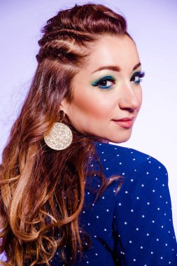 Beautiful brunette girl with make-up in blue tones, pigtails and a blue jacket posing on a background of purple